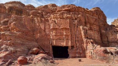 Weathered rock-cut tomb façade with a dark rectangular doorway carved into red and cream banded sandstone.