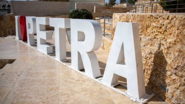 Large freestanding white PETRA letters viewed obliquely along a pale stone walkway and retaining wall.