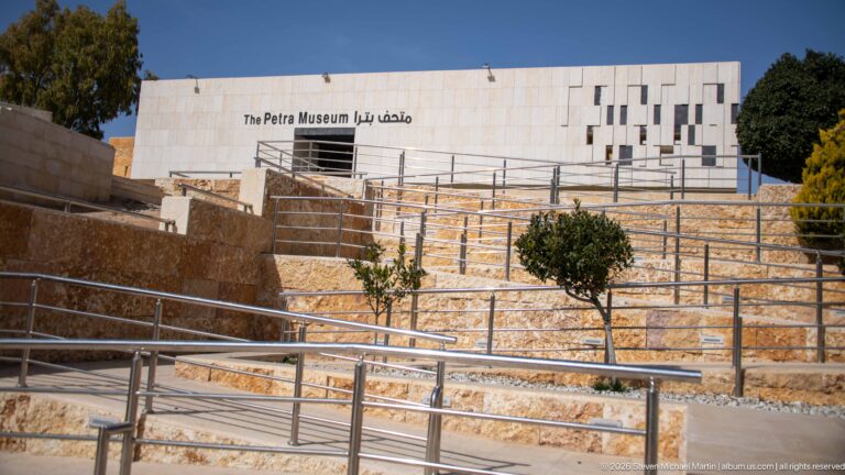 The Petra Museum behind terraced stone walls and metal ramps, with its English and Arabic name on the façade.