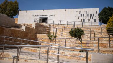 The Petra Museum behind terraced stone walls and metal ramps, with its English and Arabic name on the façade.