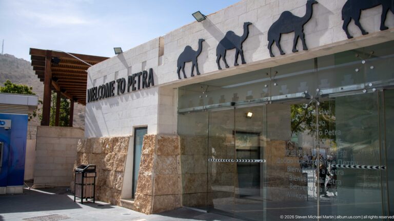 Welcome to Petra entrance with glass doors, pale stone walls, and camel silhouettes along the roofline.