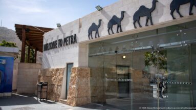 Welcome to Petra entrance with glass doors, pale stone walls, and camel silhouettes along the roofline.