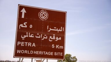 Brown bilingual road sign reading PETRA 5 Km and WORLD HERITAGE SITE beneath a heritage emblem.