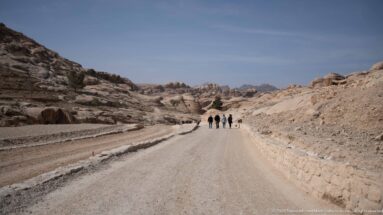 Visitors walk along a broad gravel road between low sandstone outcrops in Petra’s entrance area.