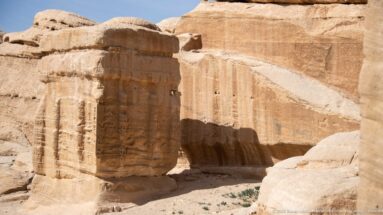 Weathered rock-cut tomb façade with shallow pilasters and horizontal moldings in Petra sandstone.
