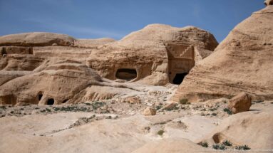 Cluster of rock-cut tombs and chambers in pale sandstone, including a stepped-crown façade at Petra.