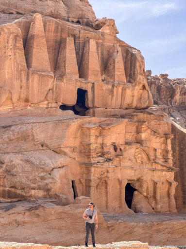 Visitor stands beneath Petra’s Obelisk Tomb, with the four-obelisk upper façade and lower openings above.