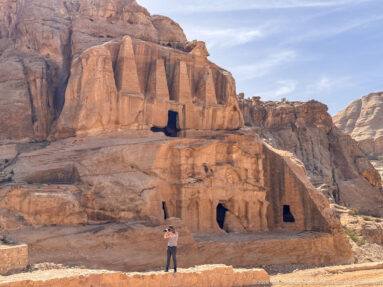 Wide view of Petra’s Obelisk Tomb above lower rock-cut chambers, with a visitor standing at the base.