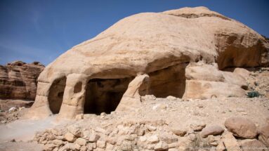 Broad dark chamber opens beneath a rounded, heavily eroded sandstone outcrop near Petra.