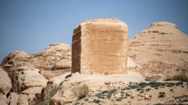 Freestanding rectangular sandstone djin block rising from a rocky outcrop near Bab as-Siq at Petra.