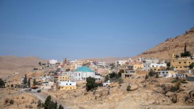 Wadi Musa hillside neighborhood with tan and white buildings clustered around a turquoise-domed mosque.