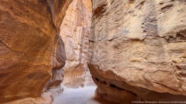 Massive weathered sandstone projection constricts the pale pathway through Petra’s Siq.