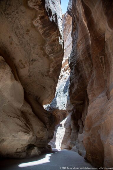 Shaded bend in Petra’s Siq beneath overhanging sandstone, with a bright narrow passage visible ahead.