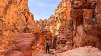 Visitor stands among towering red sandstone formations and narrow canyon passages at Petra.