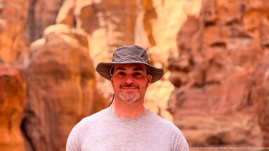 Close portrait of a smiling visitor in a sun hat against softly blurred red sandstone cliffs at Petra.