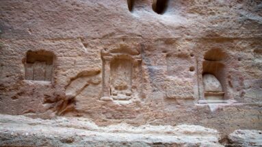 Weathered rock-cut niches and relief forms carved into the sandstone wall along Petra’s Siq.