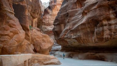 Single visitor walks through Petra’s narrow Siq between towering, banded sandstone walls.