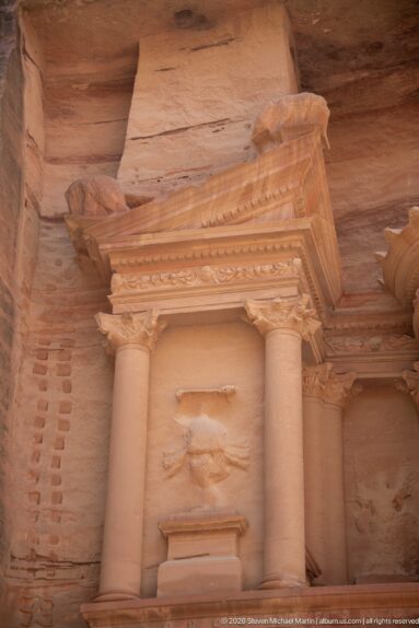Upper Treasury niche with paired columns, triangular pediment, weathered relief, and part of the central tholos.