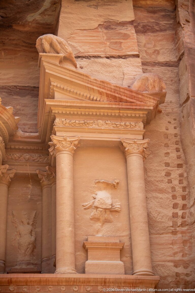 Paired columns and projecting pediment frame a weathered sculptural niche on the upper façade of Petra’s Treasury.