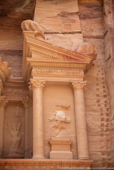 Paired columns and projecting pediment frame a weathered sculptural niche on the upper façade of Petra’s Treasury.