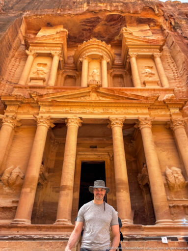 Visitor stands below the full rock-cut façade of Petra’s Treasury, with columns, pediment, and upper tholos visible.