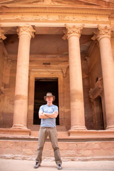 Visitor stands between massive sandstone columns before the dark central doorway of Petra’s Treasury.