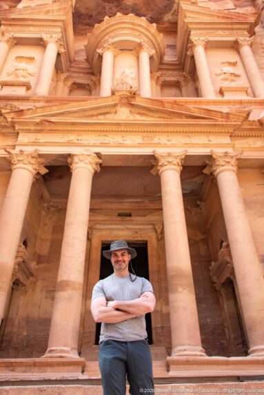 Visitor standing beneath the towering columns and dark entrance of Al-Khazneh, the Treasury at Petra.