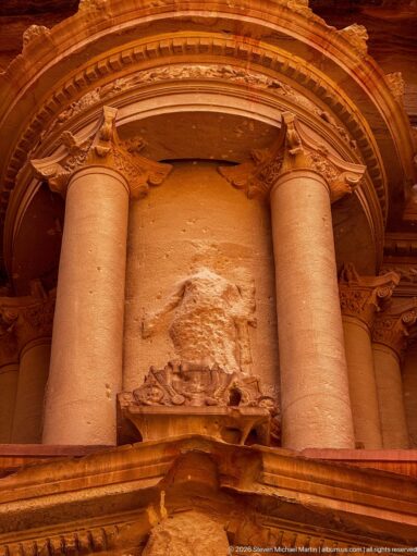 Close view of Al-Khazneh’s central upper tholos with Corinthian columns, eroded figure niche, and crowning urn.