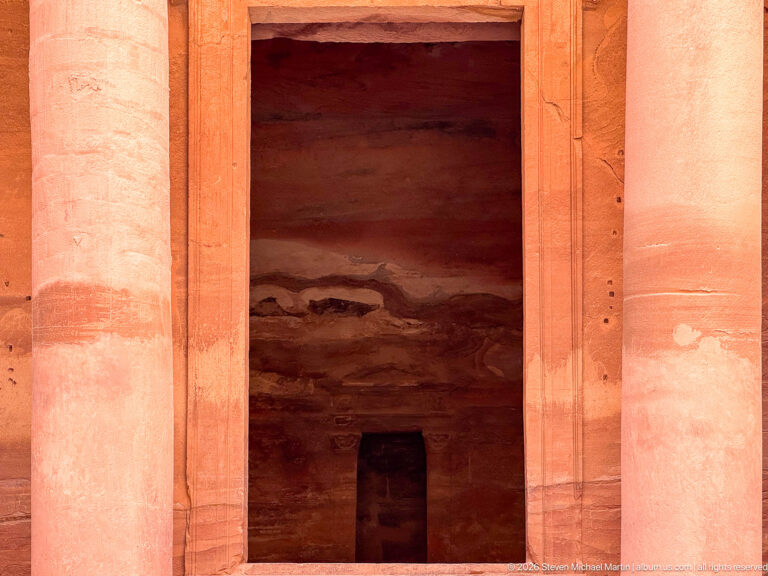 Dark entrance of Al-Khazneh framed by monumental rock-cut sandstone columns and the lower façade at Petra.