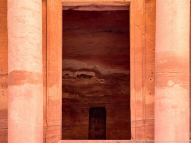 Dark entrance of Al-Khazneh framed by monumental rock-cut sandstone columns and the lower façade at Petra.