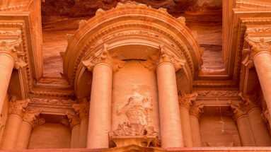 Low-angle close view of Al-Khazneh’s upper tholos, columns, broken pediments, and crowning urn carved in sandstone.