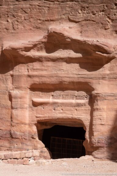 Low rectangular chamber opening with metal grille cut into horizontally banded sandstone at Petra.