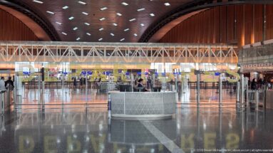 Large airport check-in hall with sweeping dark ceiling, polished floor, counters, and overhead structural truss.
