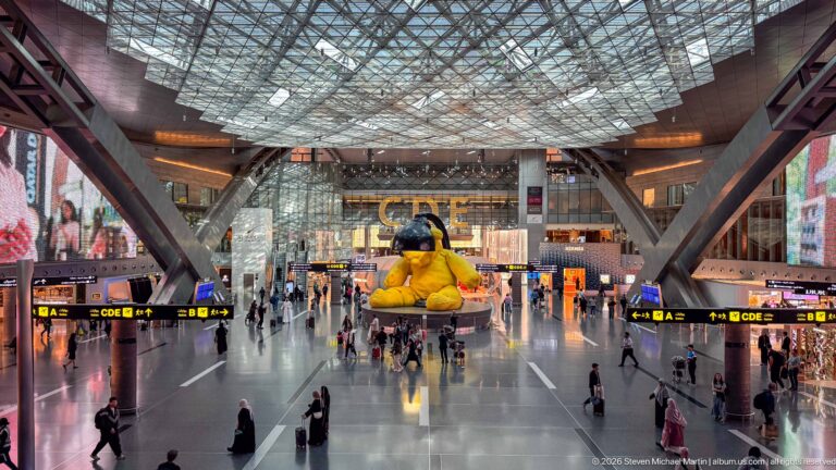 Symmetrical high view down Hamad International Airport's main concourse toward the yellow Lamp Bear.