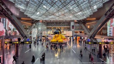 Symmetrical high view down Hamad International Airport's main concourse toward the yellow Lamp Bear.