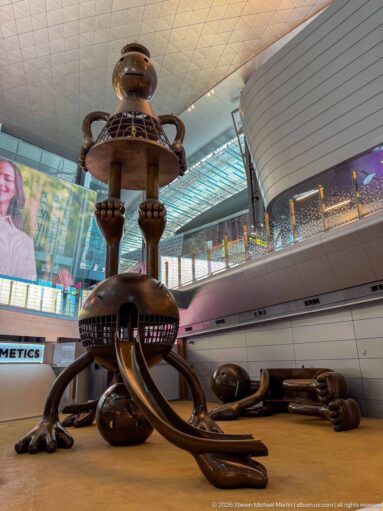 Wide low-angle view of Tom Otterness’s monumental Other Worlds installation inside Hamad International Airport.