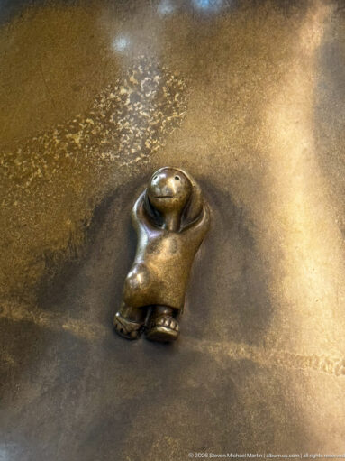 Small reclining bronze figure on a broad surface in Tom Otterness’s Other Worlds at Hamad International Airport.