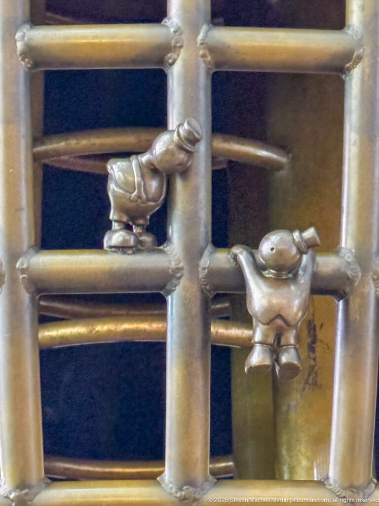 Two small bronze figures climbing a ladder-like structure in Tom Otterness’s Other Worlds at Hamad International Airport.