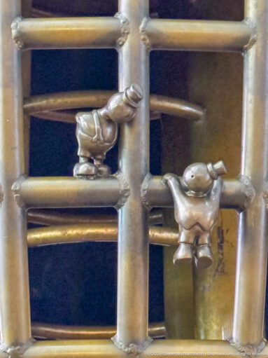 Two small bronze figures climbing a ladder-like structure in Tom Otterness’s Other Worlds at Hamad International Airport.