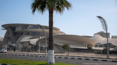 National Museum of Qatar with overlapping pale disc forms, fountains, roadway, and a tall palm in the foreground.