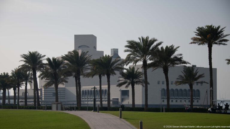 Palm-lined path and green lawn leading toward the partially obscured Museum of Islamic Art in Doha.