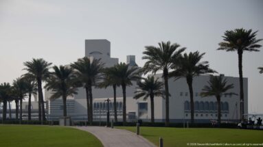 Palm-lined path and green lawn leading toward the partially obscured Museum of Islamic Art in Doha.