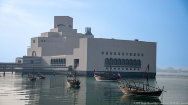 Museum of Islamic Art across calm water with several small wooden dhows in the foreground.