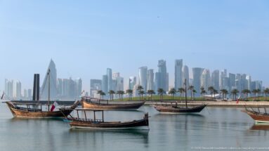 Several traditional wooden dhows on calm water with a palm-lined shore and Doha’s West Bay skyline behind.