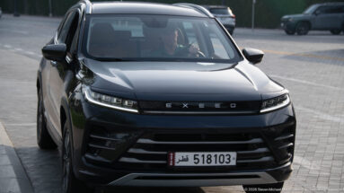 Dark EXEED SUV seen from the front with a white Qatar license plate on a Doha street.
