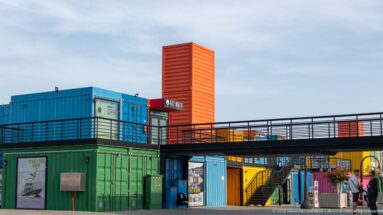 Colorful stacked shipping-container shops linked by a black elevated walkway and staircase at Box Park in Doha.