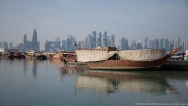 Wooden dhows moored in calm harbor water with protective canvas and Doha’s West Bay skyline in the distance.