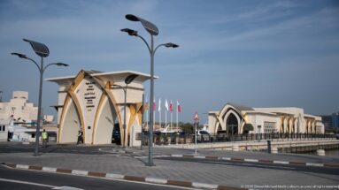 Pointed-arch gateway and pale waterfront buildings with patterned panels and gold-toned supports at Old Doha Port.