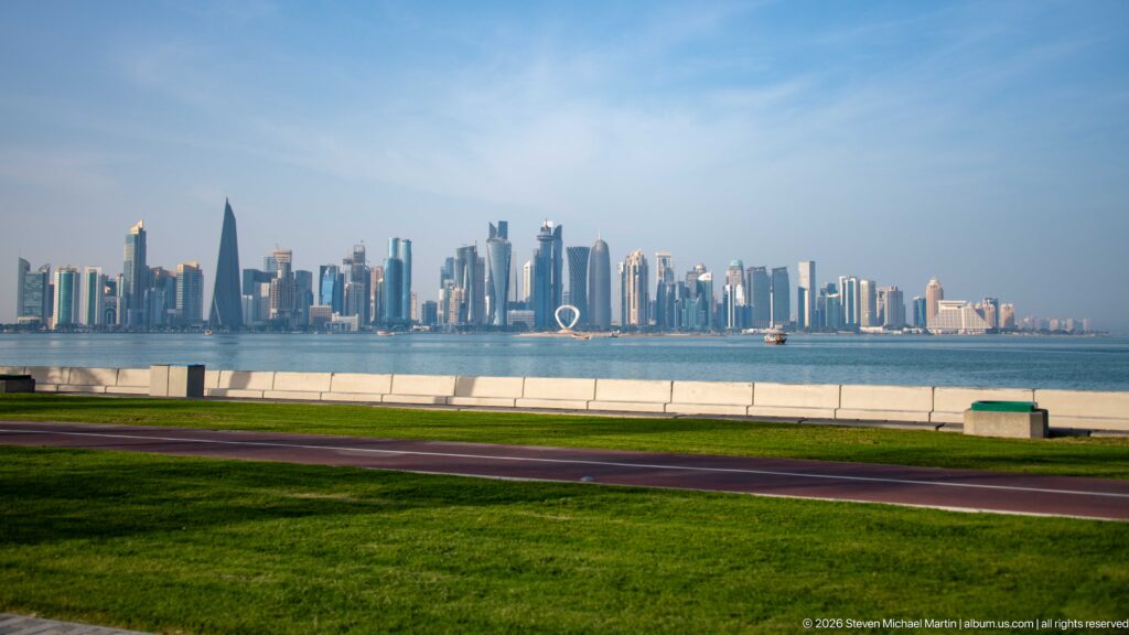 Green lawn and waterfront promenade in the foreground with Doha’s West Bay skyline across the bay.