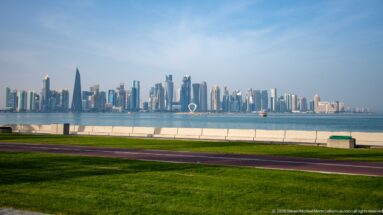 Green lawn and waterfront promenade in the foreground with Doha’s West Bay skyline across the bay.